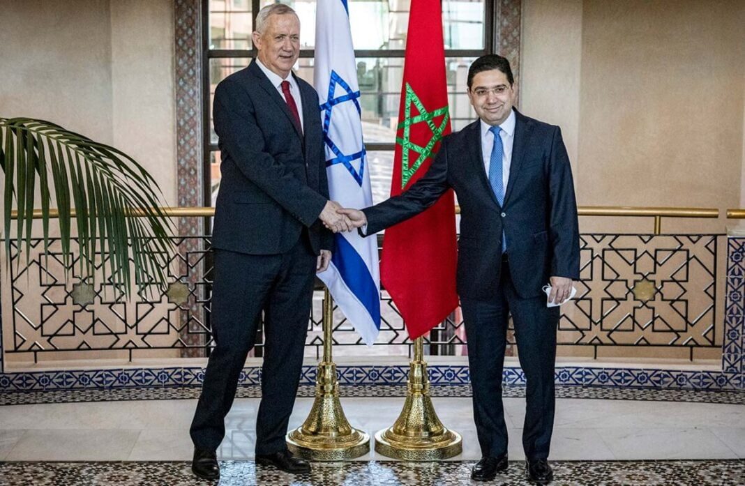 Ces hommes de main d’Israël qui réclament une guerre entre l’Algérie et le Maroc. Deux hommes d'État se serrent la main devant les drapeaux d'Israël et du Maroc.