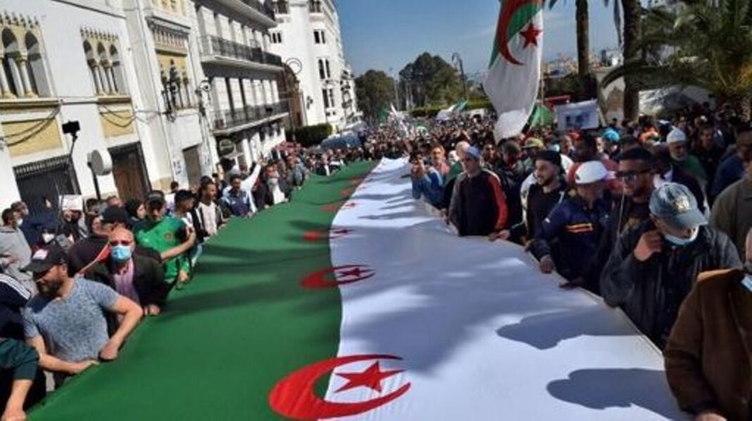 La situation des droits de l’Homme en devient « plus que jamais préoccupante » en Algérie Manifestation en Algérie avec un grand drapeau national algérien.
