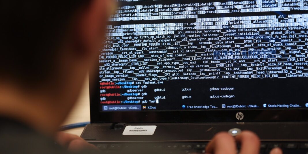 Homme surveillant un écran avec code source et alertes de sécurité.