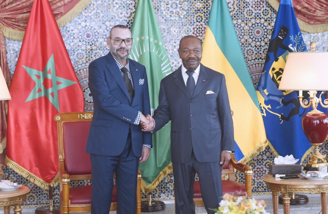 Après une longue absence… Mohammed VI apparaît au… Deux hommes en costume se serrent la main devant des drapeaux africains et marocains.