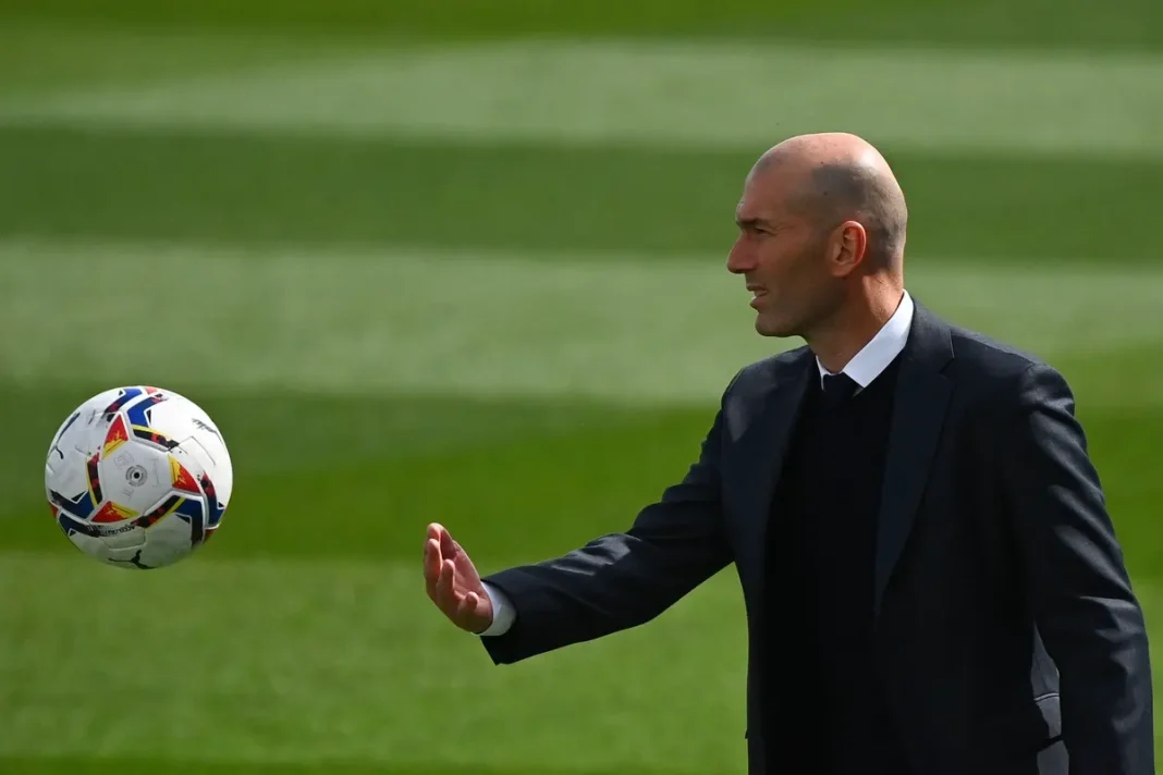 Surprenant ! Zidane use de chantage au Real de cette façon. Zidane en costume, contrôlant un ballon de football sur le terrain.