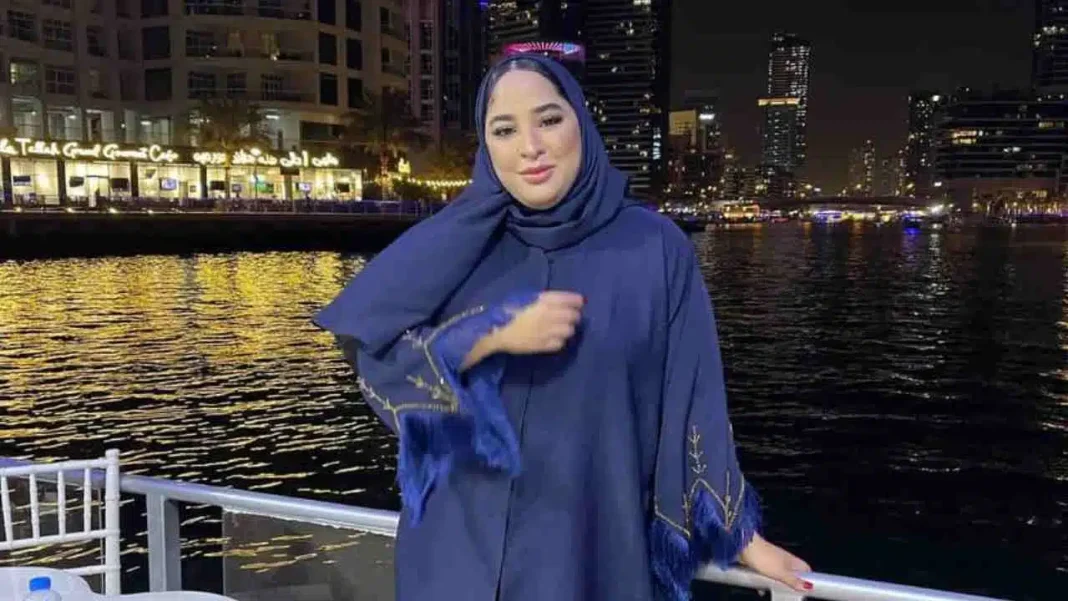 Maya Redjil portant une abaya bleue près d'une rivière urbaine.