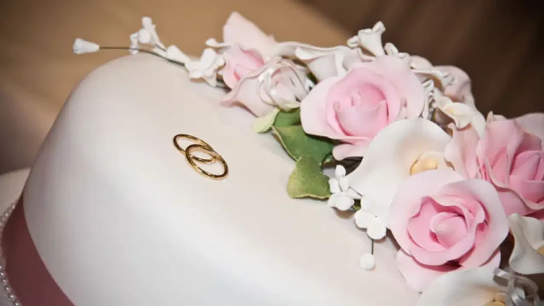 Gâteau de mariage décoré de fleurs roses Gâteau de mariage blanc avec fleurs roses et anneaux nuptiaux en or.