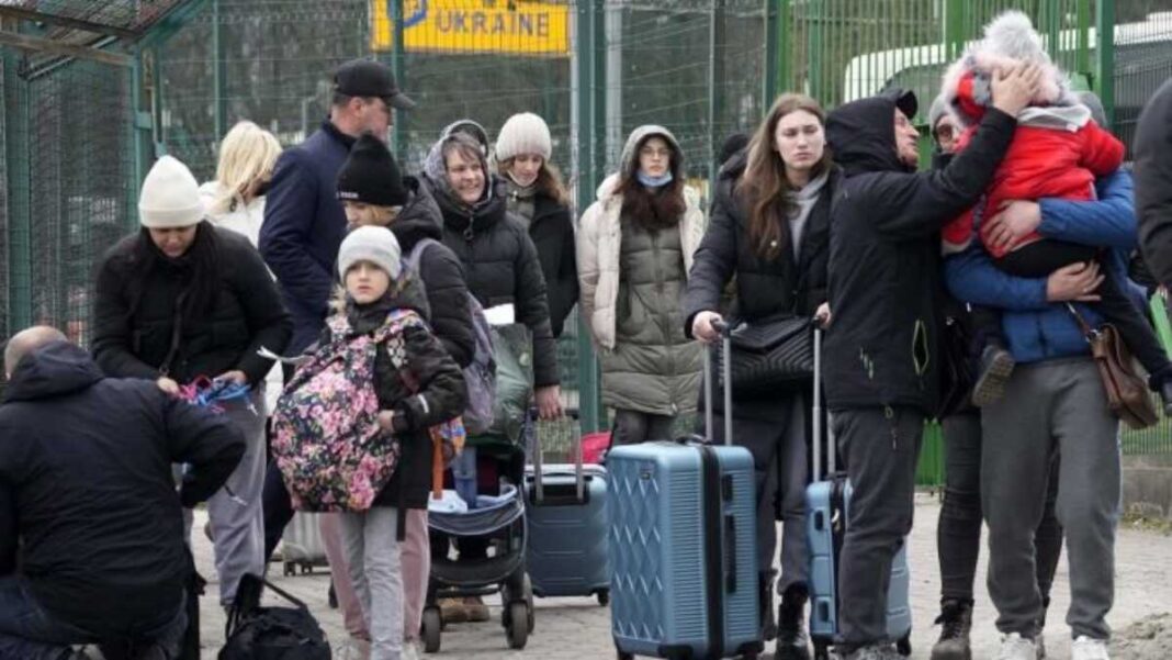 Groupe de réfugiés avec bagages devant un panneau Ukraine en France.