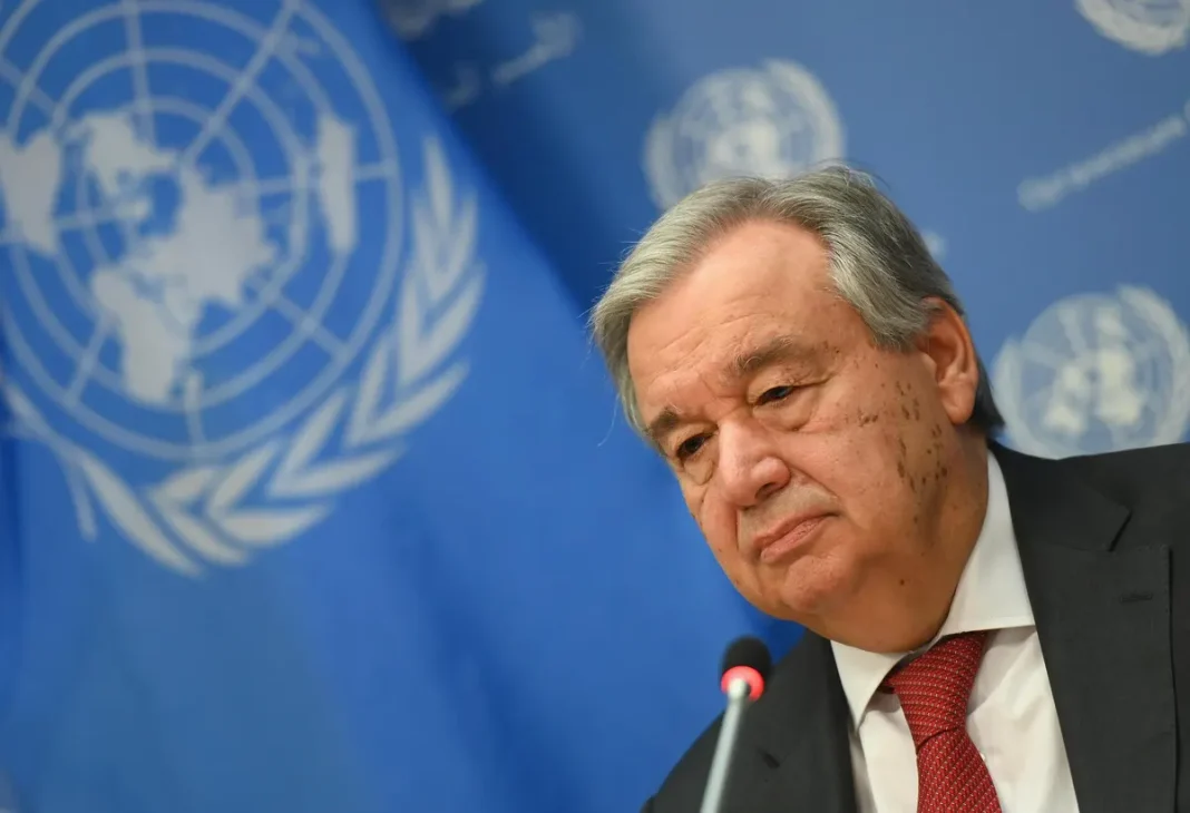 António Guterres lors d'une conférence à l'ONU avec le drapeau mondial en arrière-plan.