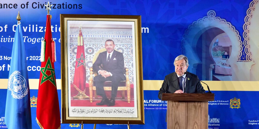 Homme parlant lors d'une conférence avec drapeau marocain et ONU en arrière-plan.