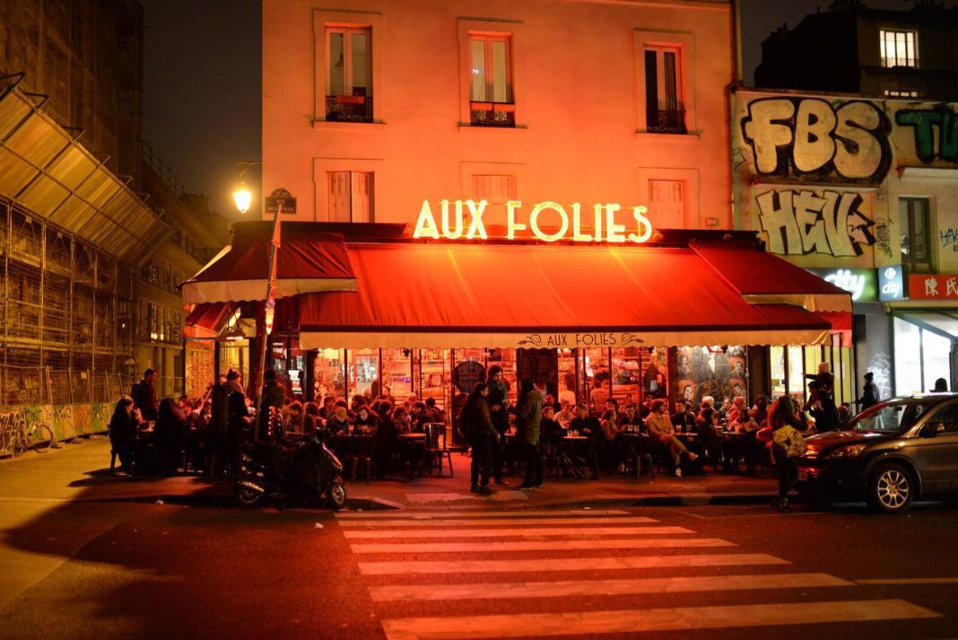 Café animé aux Folies avec clients et ambiance nocturne.