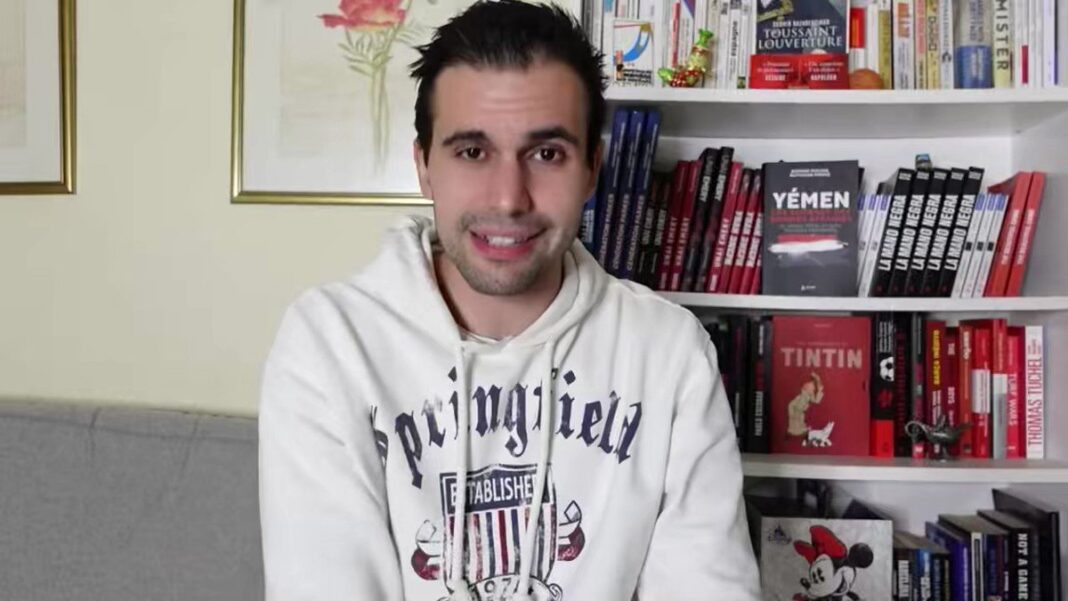 Selon Romain Molina, “ Andy Delort s’en fout de l’équipe d’Algérie” Jeune homme souriant dans une bibliothèque avec des livres en arrière-plan.