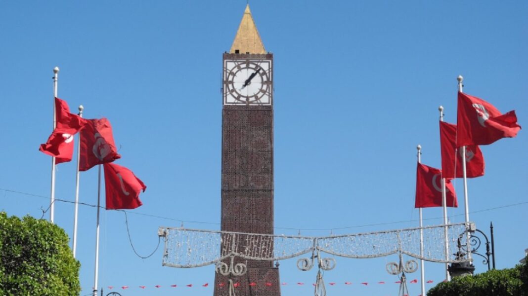 La Tunisie offre des bourses et des allocations mensuelles aux étudiants algériens inscrits dans ces filières. Horloge de Tunis avec drapeaux tunisiens en arrière-plan.
