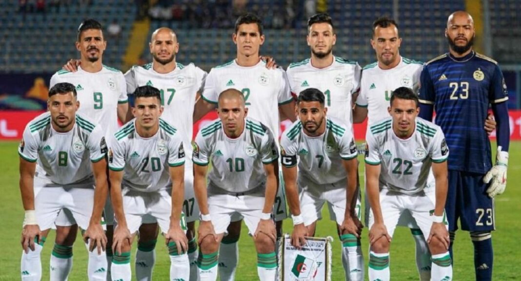 Groupe de joueurs de football algériens en tenue blanche sur le terrain.