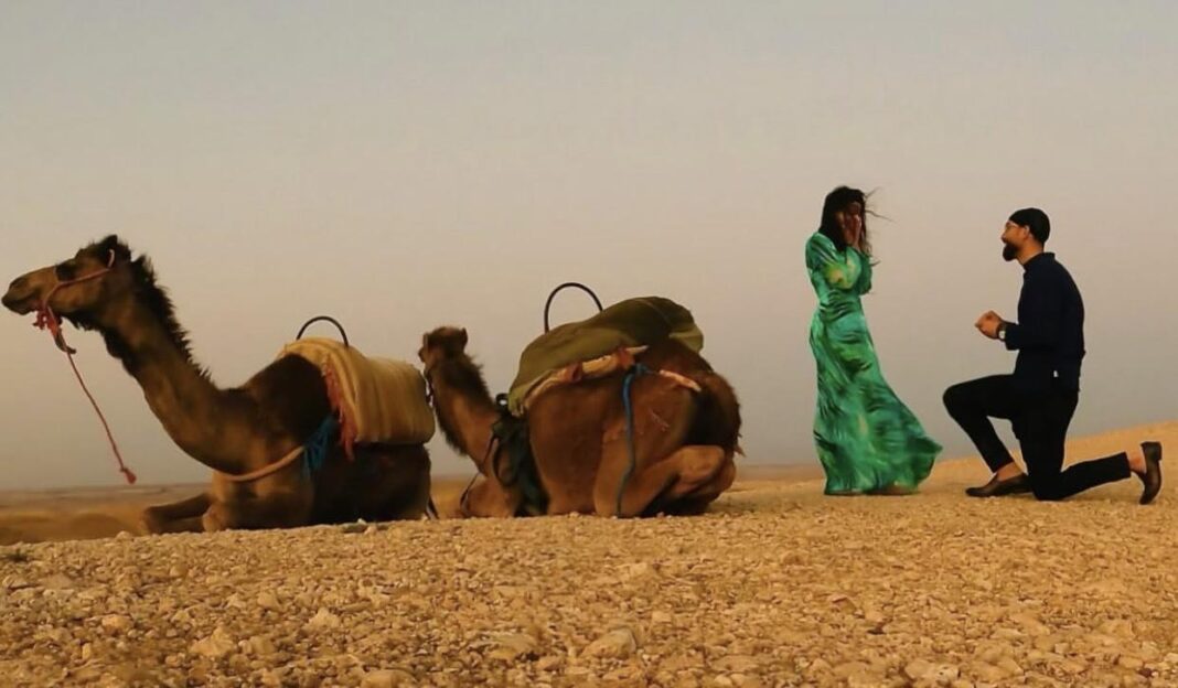 Homme faisant une demande en mariage à une femme dans le désert avec des chameaux.