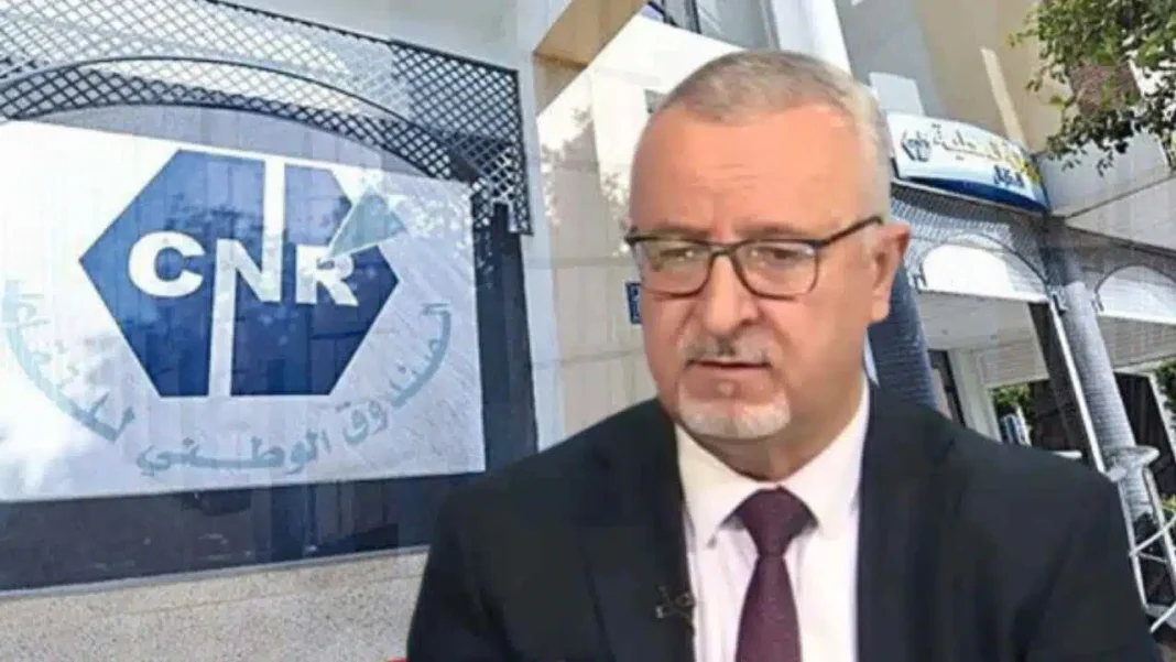 Retraite en Algérie : voici la date et le mode de versement de la hausse des pensions Homme en costume devant un bâtiment avec logo CNR en arrière-plan.