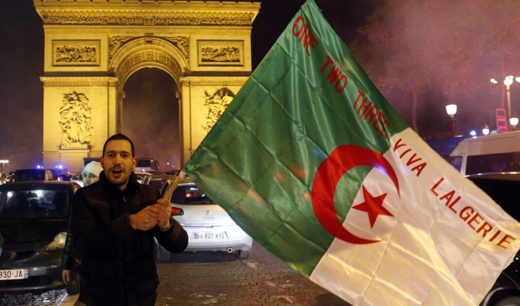 La France serait paralysé sans les Algériens : Ce haut responsable français soulève la polémique Homme tenant un drapeau algérien devant l'Arc de Triomphe à Paris.