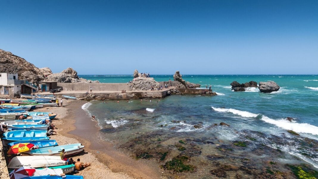 Algérie : 500 kilomètres de côtes gagnés Plage en Algérie avec bateaux et rochers, vue sur la mer Méditerranée.