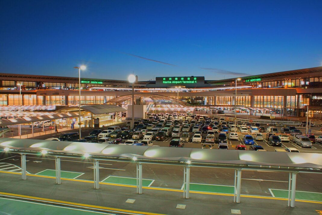 Parking d'aéroport de Nador avec voitures et terminal illuminé.