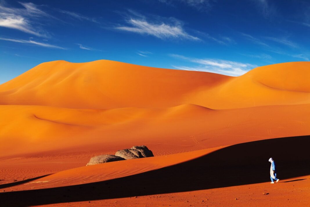 Tourisme : Voici 2 souvenirs avec lesquels vous quitterez l’Algérie. Paysage désertique avec dunes orange et ciel bleu clair.
