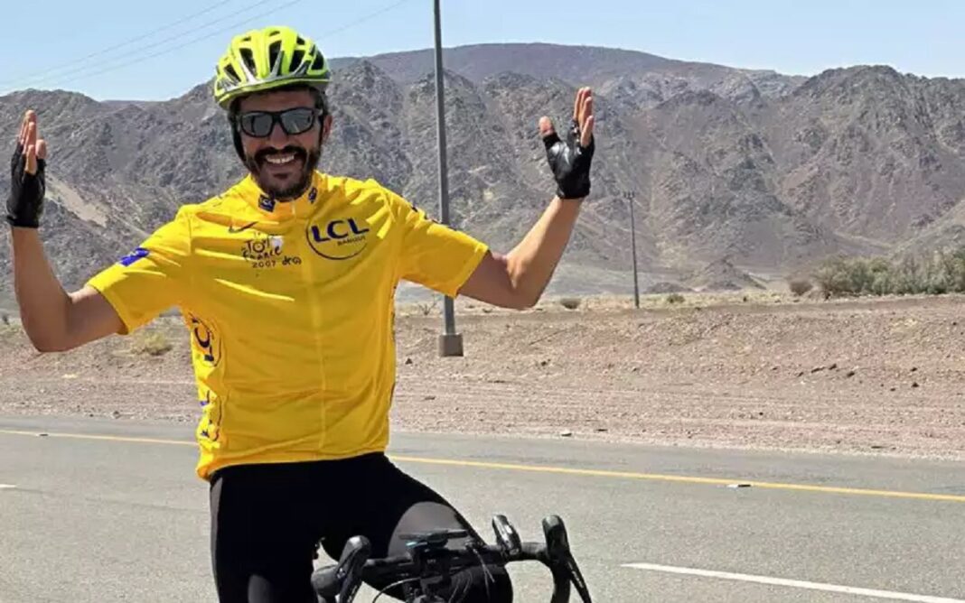 Ahurissant ! Nabil Ennasri a rejoint la Mecque à vélo depuis Paris Cycliste en route vers La Mecque, portant un casque jaune et un maillot jaune.