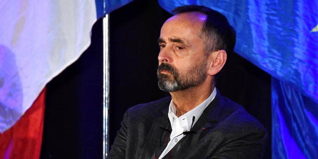 Affaire du mariage annulé d’un Algérien à Béziers : Audition imminente de Robert Ménard par la police judiciaire Homme politique avec drapeau en arrière-plan lors d'un discours.