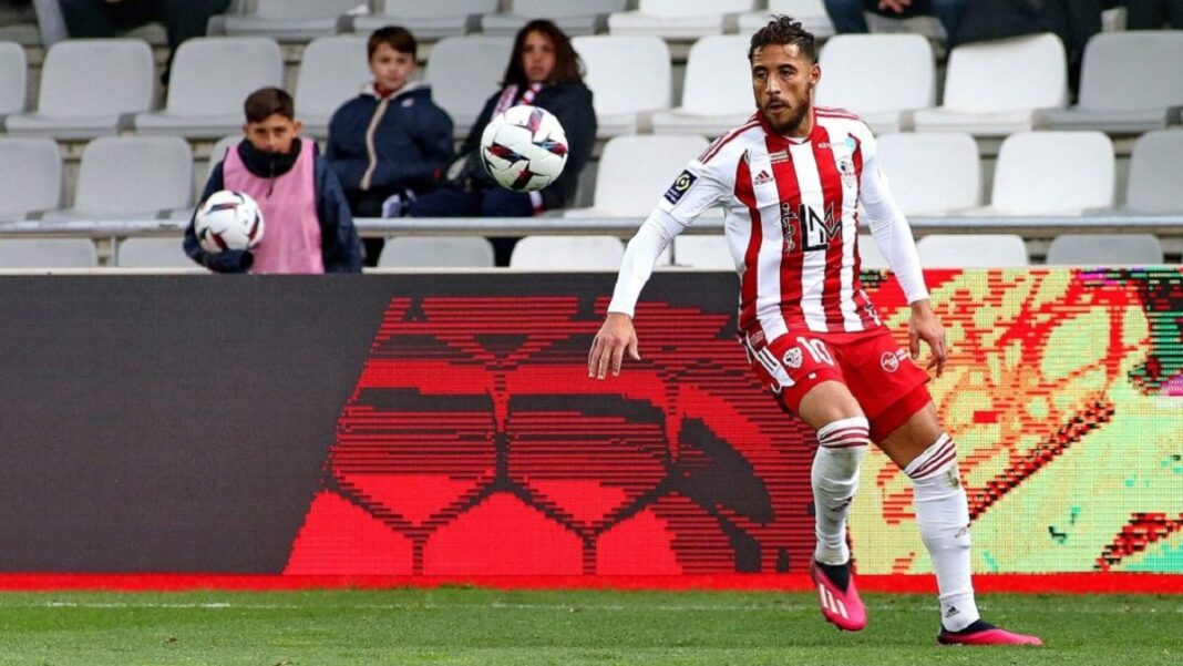 Ça n’en finit pas ! Encore un autre coéquipier de Youcef Belaili décrie le comportement du Fennec. Footballeur en mouvement sur le terrain avec supporters en arrière-plan.