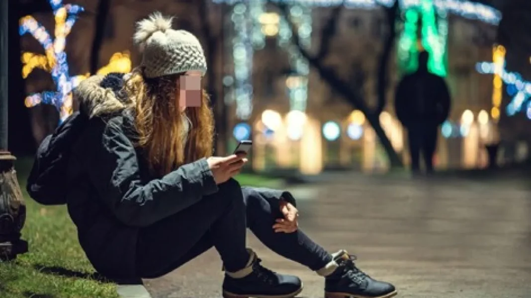 Jeune femme sans-abri utilisant son téléphone dans un parc illuminé.