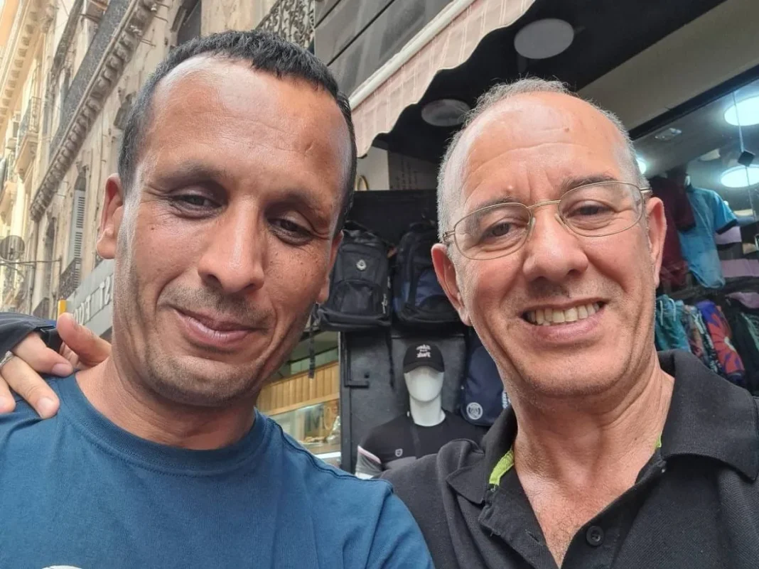 Deux hommes souriants posent pour une photo en ville.
