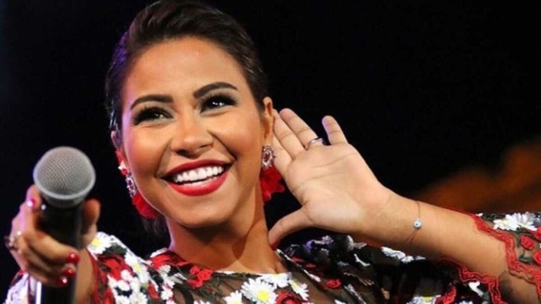 Sherine Abdel Wahab tente de se suicider Chanteuse souriante lors d'un concert, portant une robe colorée et des boucles d'oreilles.