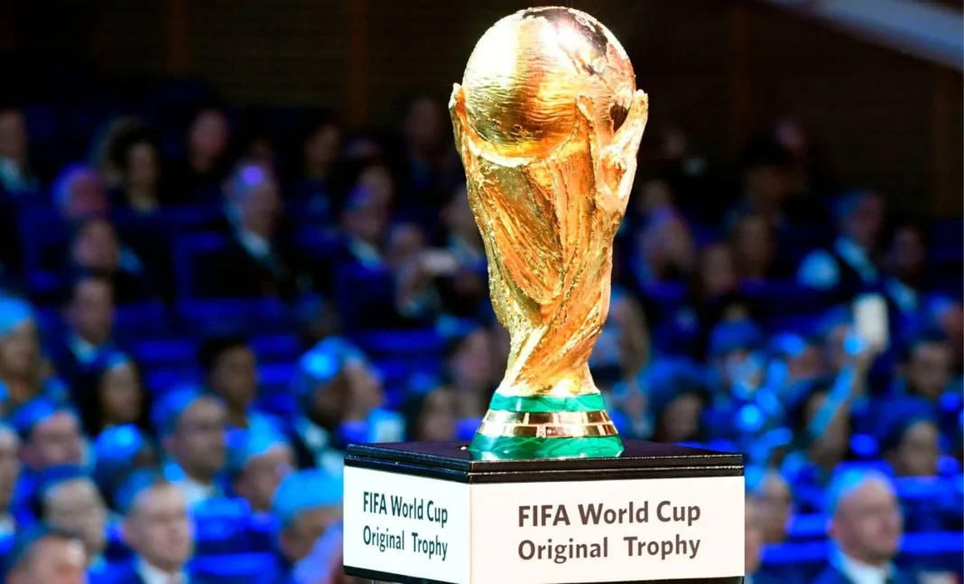 Trophée de la Coupe du Monde FIFA 2026 Trophée de la Coupe du Monde FIFA 2026 sur un socle avec public en arrière-plan.