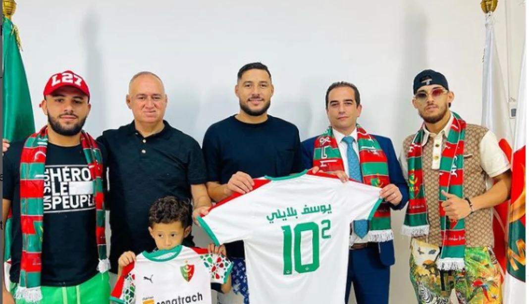 Officiel! Youcef Belaili pose ses valises au Mouloudia d’Alger Youcef Belaili pose avec des supporters et un maillot du Mouloudia d'Alger.