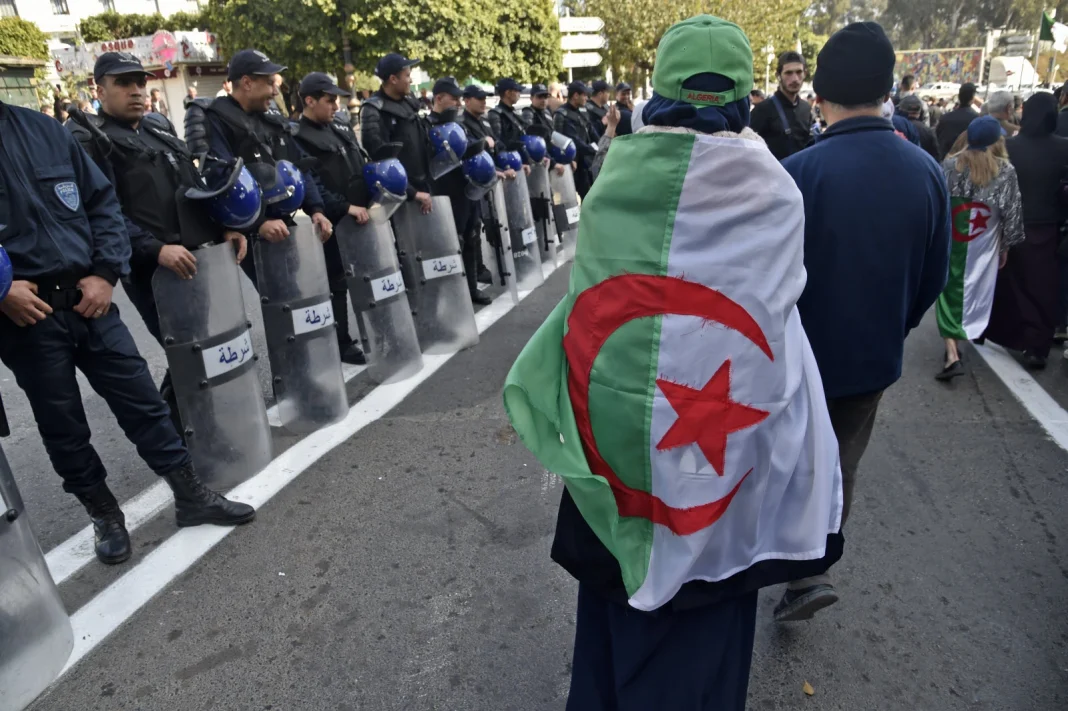 Encore un “coup de poignard dans le dos” des Algériens de France Manifestation avec un homme portant un drapeau algérien.