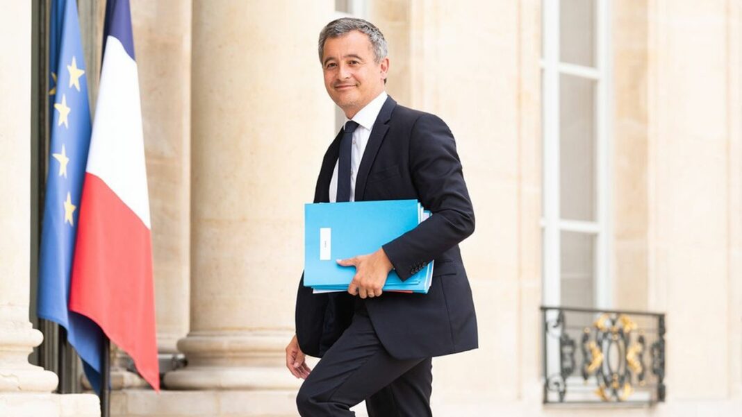 Scandale Anti-Français : Gérald Darmanin exige le retrait du titre de séjour d’un Imam Tunisien Homme politique français avec drapeaux français et européen en arrière-plan.