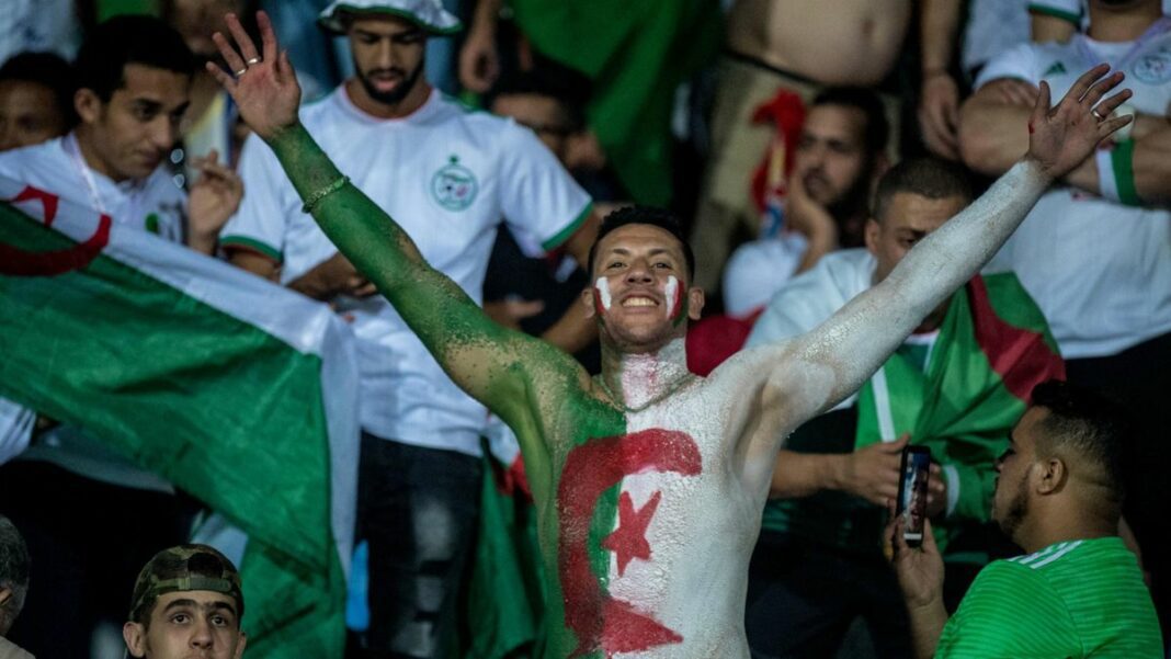 Supporter algérien avec drapeau et maquillage aux couleurs nationales.