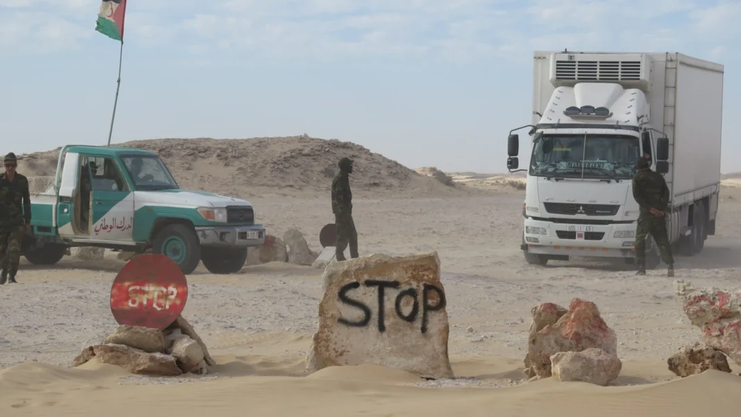 Militaires et véhicules dans un désert avec des panneaux Stop et Stop en arabe.