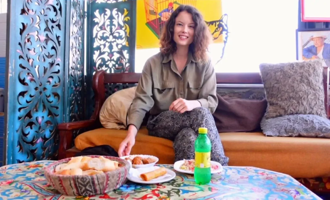 Enfin!L’influenceuse qui avait un problème de visa pour l’Algérie, a trouvé gain de cause Jeune femme souriante avec snack et boisson dans un salon coloré.