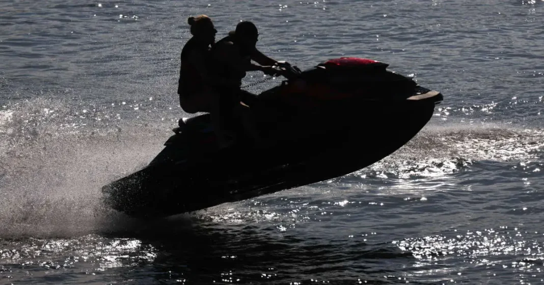 Deux personnes sur un jet-ski en mer, créant des vagues.