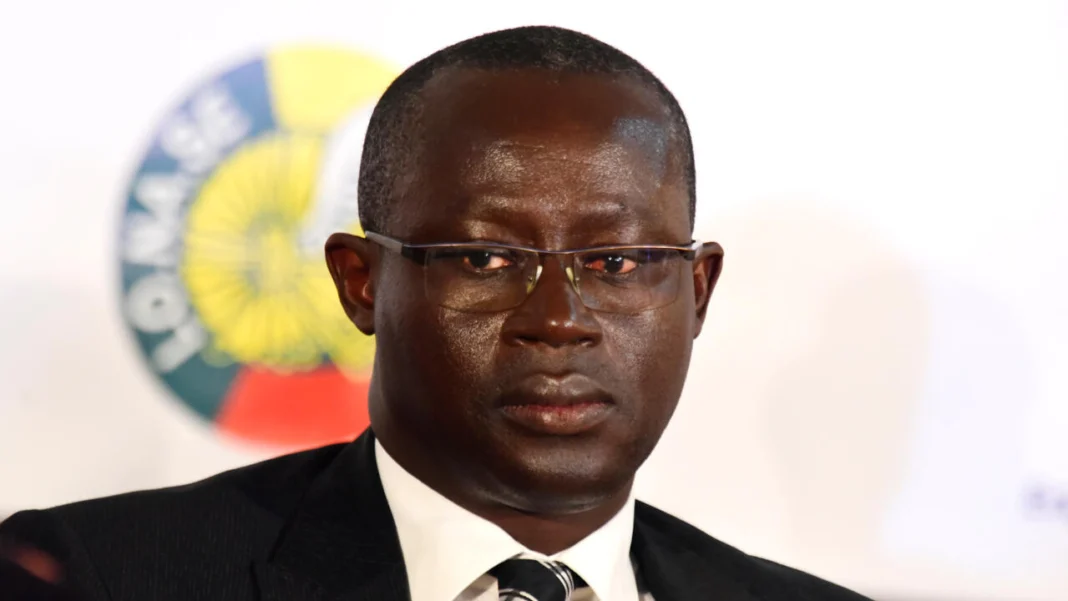 Augustin Senghor lors d'une conférence, portant costume et lunettes.