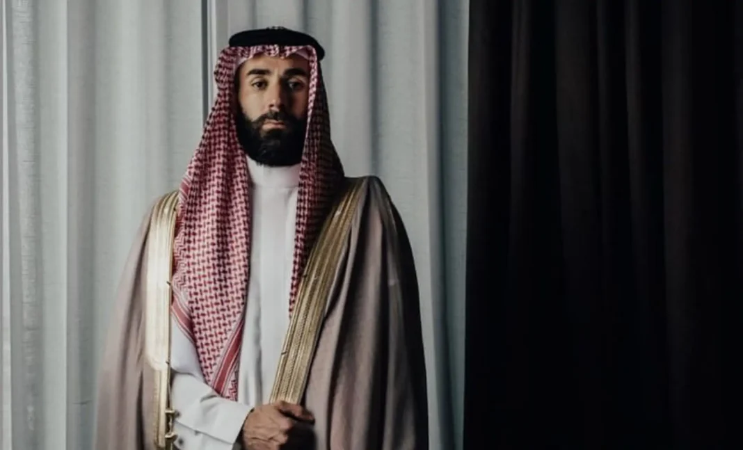 Benzema en tenue traditionnelle saoudienne, regard sérieux, fond noir et blanc.