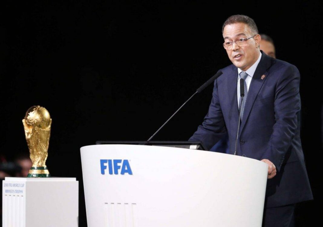 Fouzi Lekjaa parlant lors d'une conférence FIFA avec la Coupe du Monde à côté.