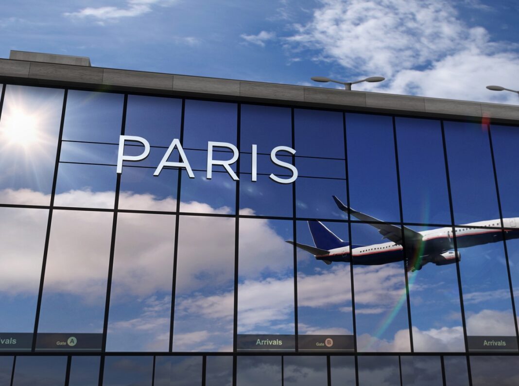 Vue d'un avion en vol reflété sur la façade vitrée de l'aéroport de Paris.
