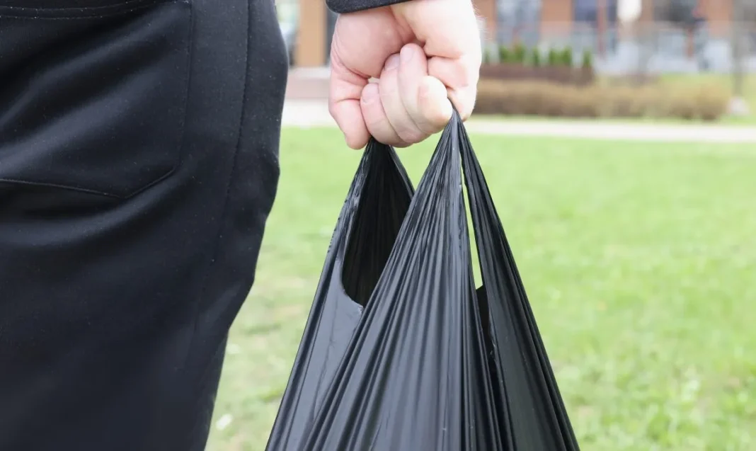 Retour des sachets noirs en plastique en Algérie : Débat sur la santé et l’environnement Main tenant un sachet noir en plastique dans un parc en Algérie.