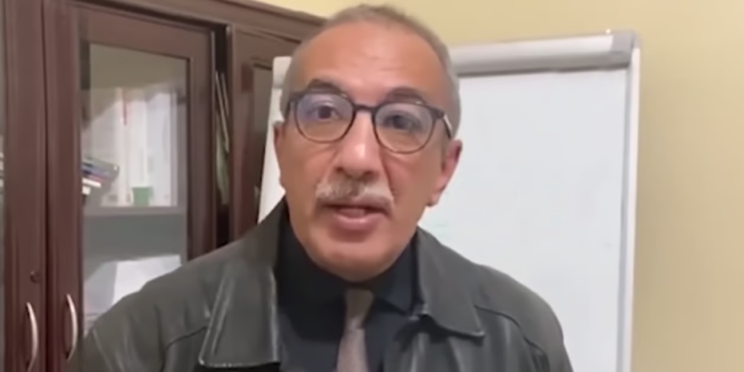 El Kadi Ihsane lors d'une interview, visage sérieux et lunettes.