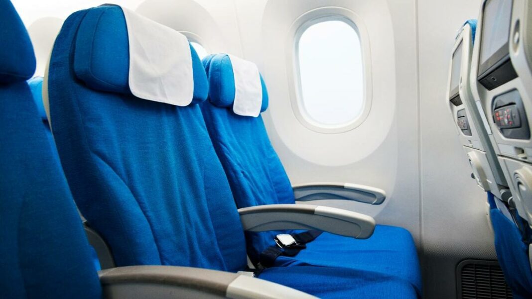 Voyage en avion : une passagère subit une situation gênante suite à l’intervention d’un steward en plein vol (Vidéo) Sièges d'avion bleus avec appuie-tête blancs dans la cabine.