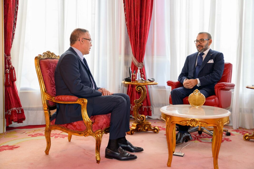 Mohammed VI désigne Fouzi Lekjaa Président du « Comité Coupe du Monde 2030 » Deux hommes en costume discutent dans un salon élégant.