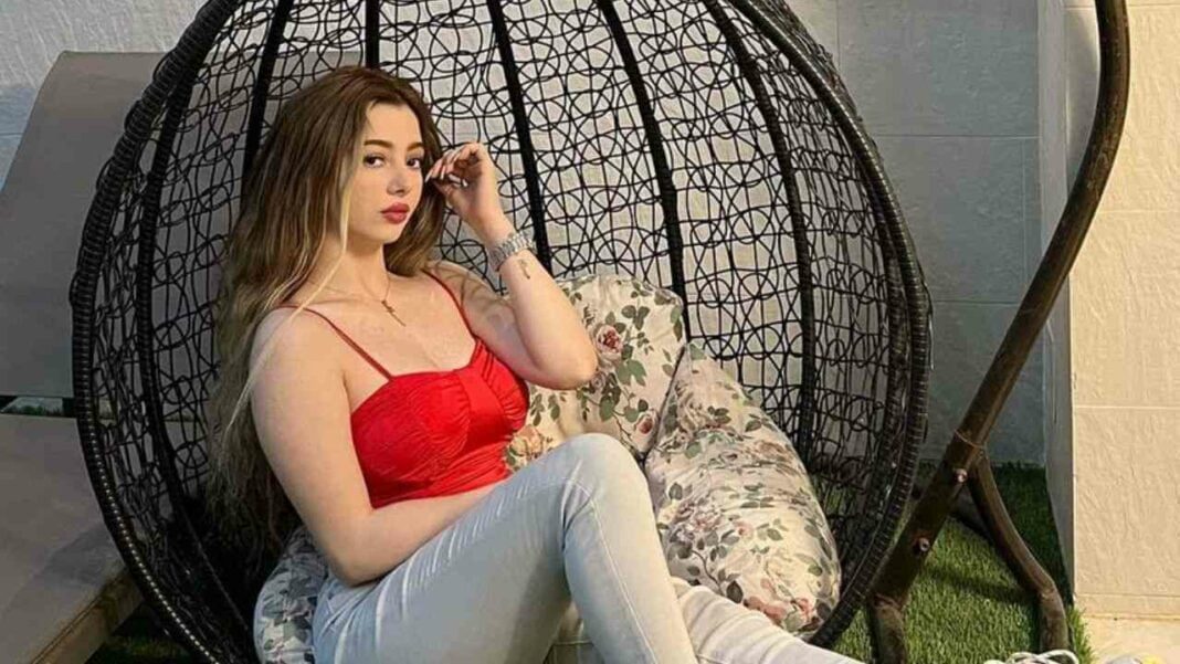 Mouna Limam, l’Influenceuse Algérienne qui surprend ses fans en Jilbeb (photo) Jeune femme en Jilbeb rouge et pantalon blanc, assise dans un fauteuil suspendu.