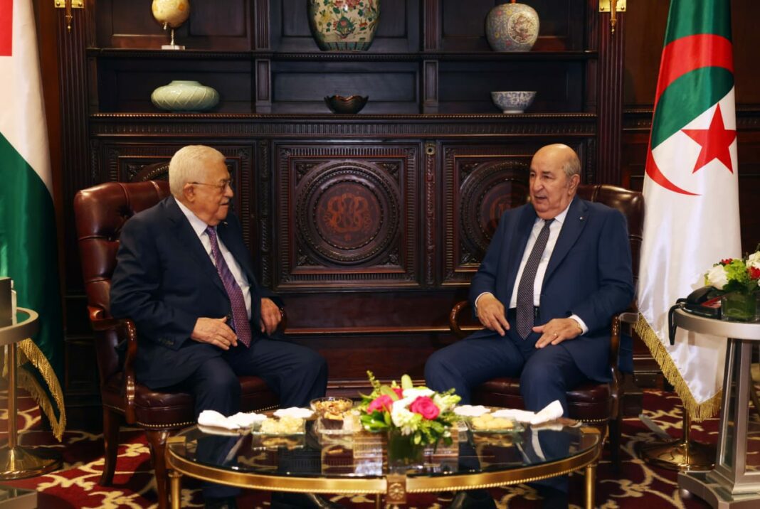 Tebboune dénonce l’Agression à Ghaza comme un Crime de Guerre Deux hommes en costume discutent dans un bureau officiel algérien.