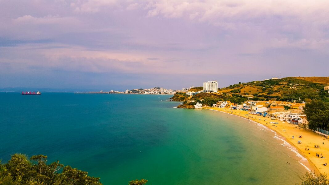 Algérie : Un aventurier dénonce la privatisation des plages, un défi pour le tourisme Vue panoramique d'une plage algérienne avec mer et côte en arrière-plan.