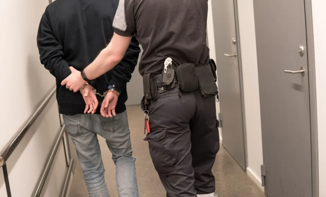 Policier menottant un homme dans un couloir d'immeuble.