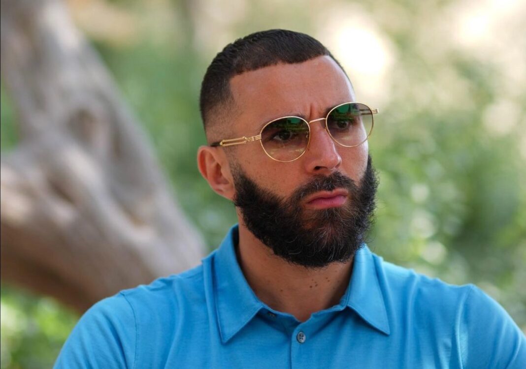 Gérald Darmanin demande à Karim Benzema de témoigner son soutien à la France Homme portant lunettes de soleil et chemise bleue.