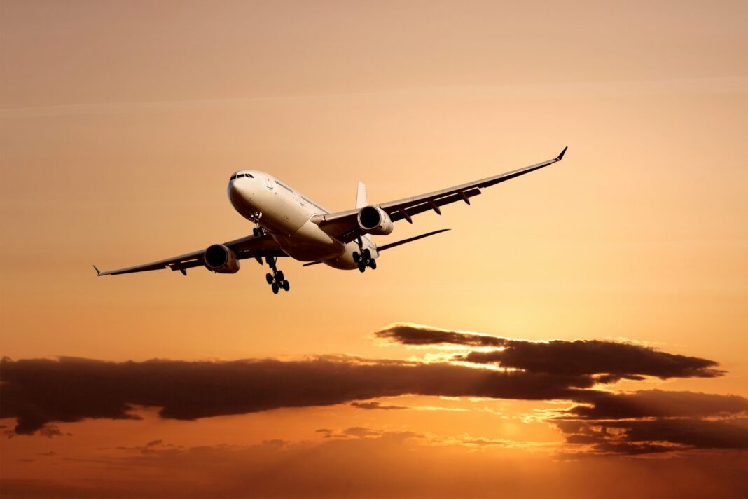 Avion commercial en vol avec ciel orange au coucher du soleil.