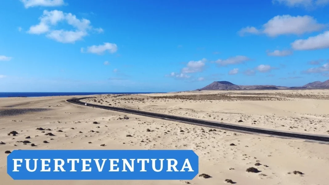 Espagne: A la découverte de l’île de Fuerteventura, une merveille insoupçonnée Plage de Fuerteventura avec ciel bleu et montagnes en arrière-plan.