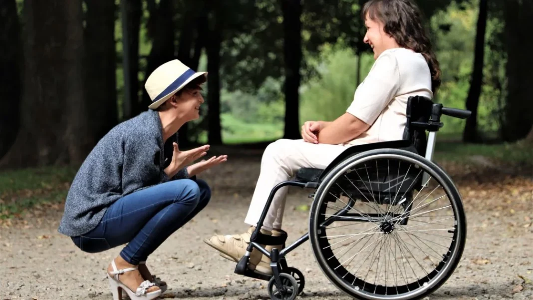 Une femme en fauteuil roulant discute avec une autre femme dans un parc.